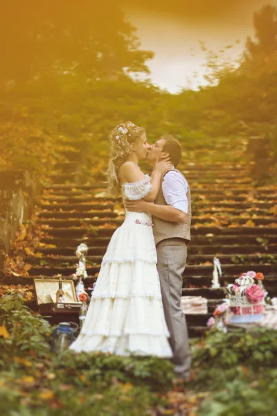 Couple de mariage dans un style rustique embrasser près des marches de pierre entourée par le décor de mariage à la forêt d'automne — Photo