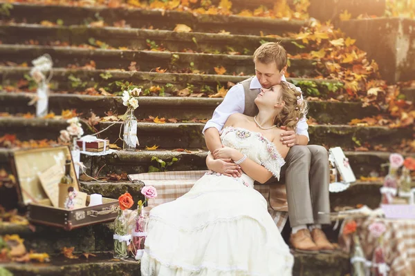 Les mariés dans un style rustique assis sur des marches de pierre à la forêt d'automne ensoleillée, entouré d'un décor de mariage . — Photo