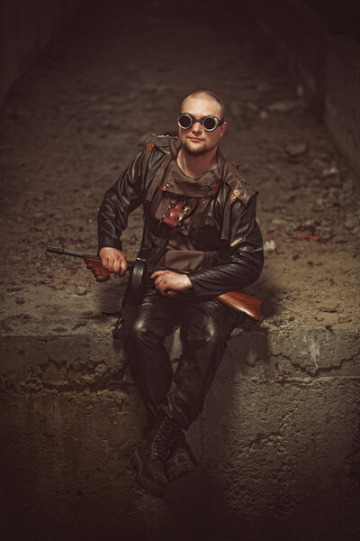 Portrait of a man from post-apocalyptic world with machine gun and the black glasses in an abandoned building