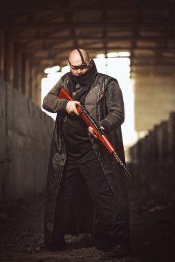 Portrait of big brutal man with rifle in leather coat as Mad Max style at abandoned building clipart