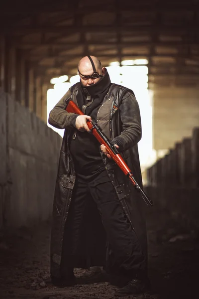 Retrato de un gran hombre brutal con rifle en abrigo de cuero como estilo Mad Max en un edificio abandonado — Foto de Stock