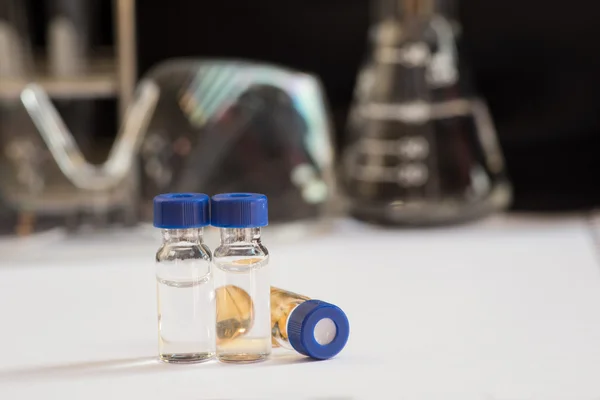 Vial de cápsula azul frente a cristalería de laboratorio —  Fotos de Stock
