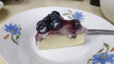 Blueberry cheesecake slice on floral plate with glossy berry topping and creamy filling, inviting dessert delight