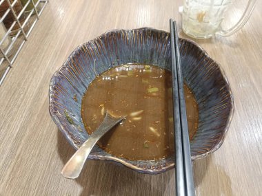 Zengin et suyu dolu boş bir kâse, metal kaşık, siyah yemek çubukları, ahşap masa, gündelik yemek, rahat bir ortam.