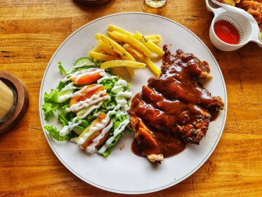 Sos soslu lezzetli bir tavuk bifteği, yanında taze salata ve altın patates kızartması servis edilir. Restoran ve yemek blogu içeriği için mükemmeldir..