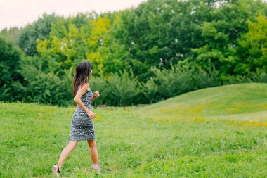 Genç kız ağaçlar boyunca parkta koşuyor.