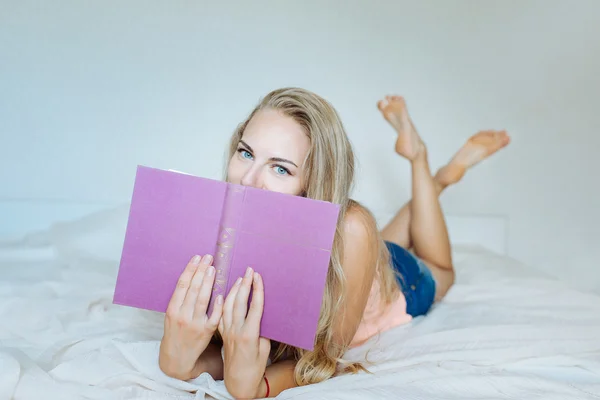 Das Mädchen auf dem Bett mit einem Buch lizenzfreie Stockbilder