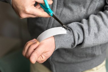 El işi için gri kazak kolundaki beyaz bandı kesmek için makas kullanan şahıs. Boşluğu kopyala