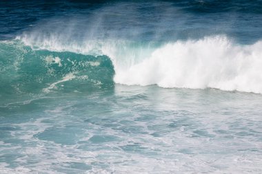 Kıyıdaki okyanus dalgaları beyaz köpük ve turkuaz su üreterek kıyı ortamında güneş ışığının yüzeyden yansımasıyla kırılır.