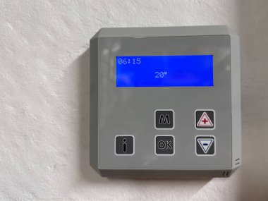 Çağdaş bir kapalı ortamda beyaz bir duvara monte edilmiş mavi ekran zaman ve sıcaklık ayarları ile dijital termostat