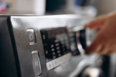 Çamaşır makinesinin kontrol düğmesini çeviren bir elin yakın görüntüsü, dijital ekran ve arkaplanda çeşitli düğmeler