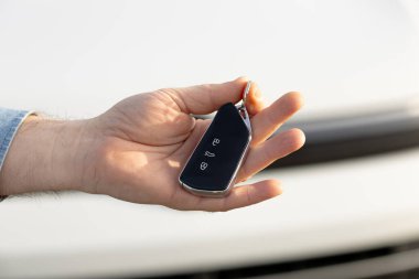 Araba galerisi. Elde düğmeleri olan, bulanık bir araç kaputuna ayarlanmış, otomotiv sahipliğini ve erişilebilirliğini vurgulayan gösterişli bir anahtar düğmesi var