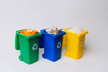 Yeşil, mavi ve sarı üç geri dönüşüm kutusu, sade beyaz arka planda organik atık, kağıt ve plastikle dolu.