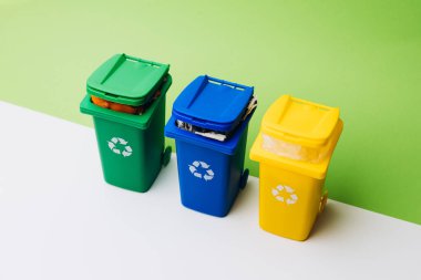 Atık ayırma ve çevresel sorumluluğun önemini vurgulayarak, temiz bir yüzeye canlı renklerde üç geri dönüşüm kutusu yerleştiriliyor