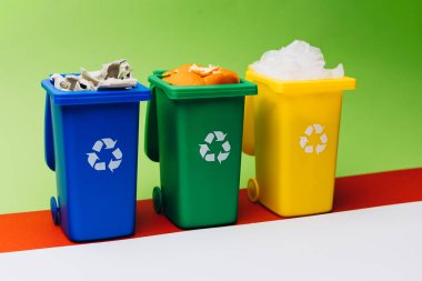 Çevre dostu uygulamaları vurgulayarak ve geri dönüşüm önemini vurgulayarak, çeşitli atık maddelerle dolu, mavi, yeşil ve sarı üç geri dönüşüm kutusu