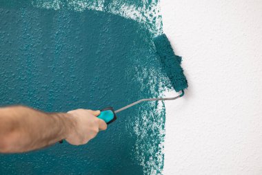 El desenli bir duvara boya sürmek için bir boya silindiri kullanıyor, tasarım için geniş bir kopya alanına sahip bir ev geliştirme projesini gösteriyor