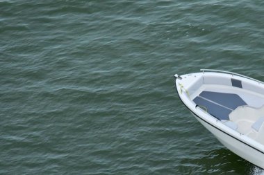 The front of a sleek, white motorboat on dark green water, creating a minimalist background with plenty of open copy space for design.