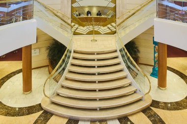 Venice. Italy - October 15, 2025: Atrium of a luxury cruise ship with an imposing symmetrical marble staircase. Glass and brass railings reflect the opulence of the interior design.