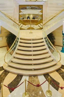 Venice. Italy - October 15, 2025: Vertical view of an elegant marble and brass staircase on a cruise ship. In the background, a reception desk with staff ready to assist guests.