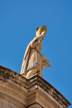 Aziz Blaise 'in altın eldiven taktığı ve çapraz tutuş yaptığı yakın plan bir fotoğraf. Bu heykel, kültürel mirasın ve Eski Şehir 'e olan inancın önemli bir sembolüdür..