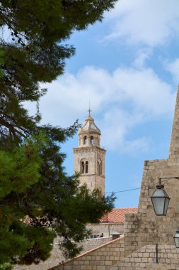 Dubrovnik. Hırvatistan - 04 Kasım 2025: Hırvatistan 'ın Dubrovnik kentindeki Fransisken Manastırı çan kulesinin dikey görüntüsü. Tarihi taş kule bir çam ağacı ve şehir duvarları tarafından çerçevelenmiş..