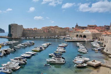 Dubrovnik. Hırvatistan - 04 Kasım 2025: Dubrovnik 'teki eski limana canlı bir bakış açısı. Tekneler antik şehir duvarları ve St. Johns Kalesi 'nin yanındaki turkuaz sularda demirli. Arka planda terracotta çatıları.