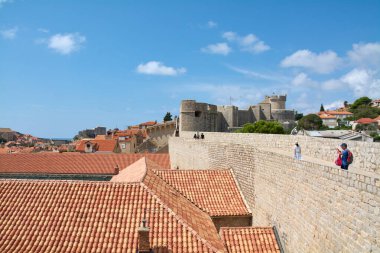 Dubrovnik. Hırvatistan - 08 Kasım 2025: Turistler, güneşli bir günde eski kentin ve Minceta Kulesinin kırmızı çatılarına bakan tarihi taş kent duvarlarında yürüyorlar