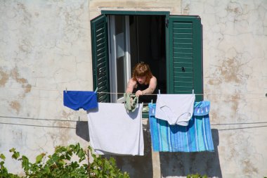 Dubrovnik. Hırvatistan - 17 Kasım 2025: Hırvatistan 'da günlük yaşamın samimi bir anı. Bir asistan ev işleri yapar, güneşli bir yaz gününde elbiselerini havaya asar..