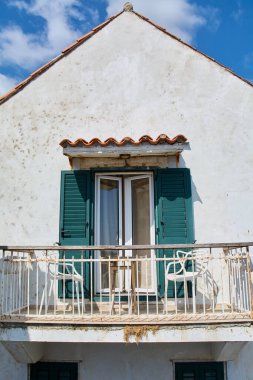 Hırvatistan 'ın Dubrovnik kentindeki eski bir binanın ön yüzü. Beyaz sandalyeli ve koyu renk panjurlu geleneksel bir balkon yıpranmış sıva duvarıyla çelişiyor..