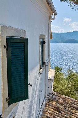 Korfu Beyaz Saray cephesi açık yeşil panjurlarla güneşli bir Corfu yaz gününde pırıl pırıl Akdeniz manzarası ve uzak tepeleri sunuyor.