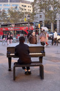 Barselona 'da. İspanya - 10 Ocak 2026: İspanya 'da güneşli bir kış öğleden sonrasında trafik ve yayalar önünde bir sokak sanatçısı piyano çalıyor.