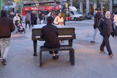 Barselona 'da. İspanya - 10 Ocak 2026: Arkasından bir piyanist yoğun bir caddede kırmızı bir turist otobüsüyle piyano çalıyor ve insanlar soğuk bir kış akşamında geziniyor.