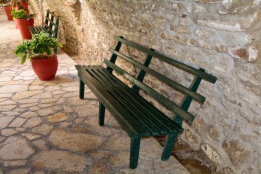 Akdeniz 'de bir ara sokakta taş bir duvarın yanında boş yeşil banklar, sakin seyahat havasını, kırsal mimariyi ve açık hava alanını aktarıyor..