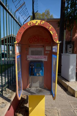Korfu. Yunanistan - 29 Ocak 2026: Açık havada Yunan tabelası ve grafitiyle yıpranmış ankesörlü telefon kulübesi, yaşlanan telekom altyapısı, kentsel bozulma ve Yunanistan 'daki haberleşme alışkanlıklarını yansıtıyor.