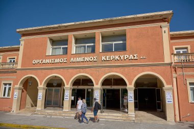 Korfu. Yunanistan - 02 Şubat 2026: Ziyaretçiler Korfu Liman İdaresi binasının önünden Yunan tabelasıyla ve kemerli girişle geçerek resmi deniz idaresi, seyir turizmi akışı ve Akdeniz limanındaki günlük faaliyetleri temsil ediyorlar.