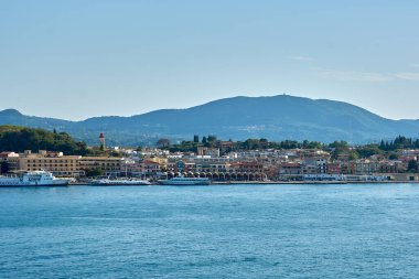 Korfu. Yunanistan - 02 Şubat 2026: Limanı, Pastel kentsel silueti ve ötesinde yeşil tepeleri bulunan Corfu şehrinin liman manzarası, İyon ada yaşamı, kıyı taşımacılığı, turizm ve günlük deniz faaliyetlerini ifade ediyor.
