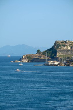 Deniz kenarı, yelkenli ve motorlu tekne derin mavi denizi geçerek tarihi savunma, deniz trafiği ve Akdeniz ada seyahatinin cazibesini birleştirir.