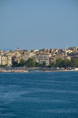 Korfu. Yunanistan - 03 Şubat 2026: Yoğun tarihi binalar, sakin mavi denizin yanındaki kilise kulesi ve kıyı yolu ile Corfu 'nun eski sahil manzarası Akdeniz kentsel yaşam ve seyahat merkezinin cazibesini ifade ediyor