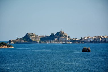 Korfu. Yunanistan - 03 Şubat 2026: Kuvvetlendirilmiş eski kent, liman direkleri ve fırtınalı gökyüzü altındaki kayalık adanın panoramik deniz manzarası, miras, esneklik, turizm ve zamansız kıyı atmosferi aktarımı