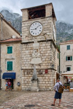 Kotor. Karadağ - 06 Şubat 2026: Akdeniz 'de bulutlu bir gökyüzünün altında tarihi saat kulesinin önünden geçen insanlar.