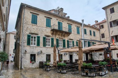 kotor. Montgomery - Şubat 07, 2026: Avrupa mimarisi, turizm ve şehir yaşam tarzını yansıtan yağmurdan sonra eski kasaba meydanında yeşil panjurlu tarihi taş binalar ve açık kafe koltuklar
