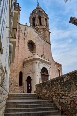 Çan kulesi ve taş merdiven ile tarihi kilise cephesi yumuşak bulutlu gökyüzünün altında yer alır..