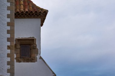 Taş çerçeveli pencereli Maricel saray köşesi detayları ve dramatik Akdeniz gökyüzüne karşı terasotta çatı fayansları