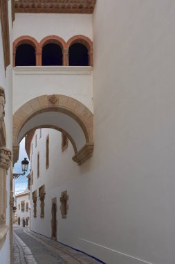 Eski kentte taş kemer ve tarihi cephelerle çerçevelenmiş dar bir ortaçağ sokağı. Geleneksel kıyı mimarisi ve sessiz Avrupa cazibesi sergileniyor.