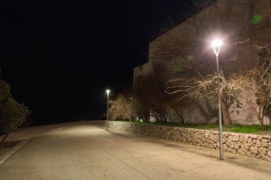 Sitges 'deki San Sebastian Mezarlığı' ndaki tarihi taş duvarlar ve aydınlatılmış selvi ağaçları gece görüşü..