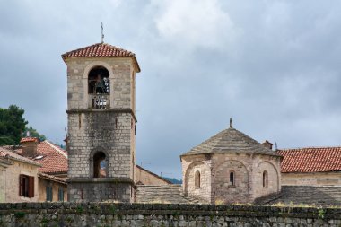 Tarihi taş çan kulesi ve ortaçağ ortodoks kilisesinin kubbeli kilisesi Akdeniz 'deki bir köyde bulutlu bir gökyüzüne karşı duruyor ve Kotor' daki geleneksel romantik mimari detayları gösteriyor.