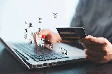 Çevrimiçi ödeme, dijital alışveriş, güvenli işlemler ve modern perakende teknolojisini temsil eden, parlayan sanal alışveriş arabası ve ekommerce simgelerine sahip bir laptop ve kredi kartı kullanan bir kişi.