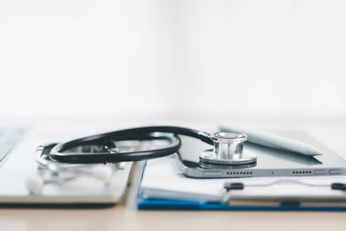 Akıllı telefondaki steteskop, parlak masa arkasında pano ve kalemle, teletıp, dijital sağlık kayıtlarını, çevrimiçi danışmanlık ve mobil sağlık sigortasını sembolize ediyor. teletıp