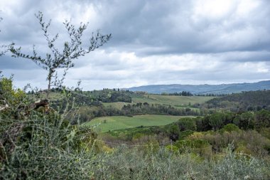 Dramatik bulutlu bir gökyüzünün altında yuvarlanan yeşil tepelerin ve vadilerin manzarası, doğanın sükunetini ve manzaranın canlı renklerini vurguluyor.