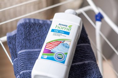 Riga, Letonya - 08 Şubat 2026: Amway Home SA8 Çamaşır deterjanı şişesi mavi havluda kurutma askısı üzerinde çizgili giysiler